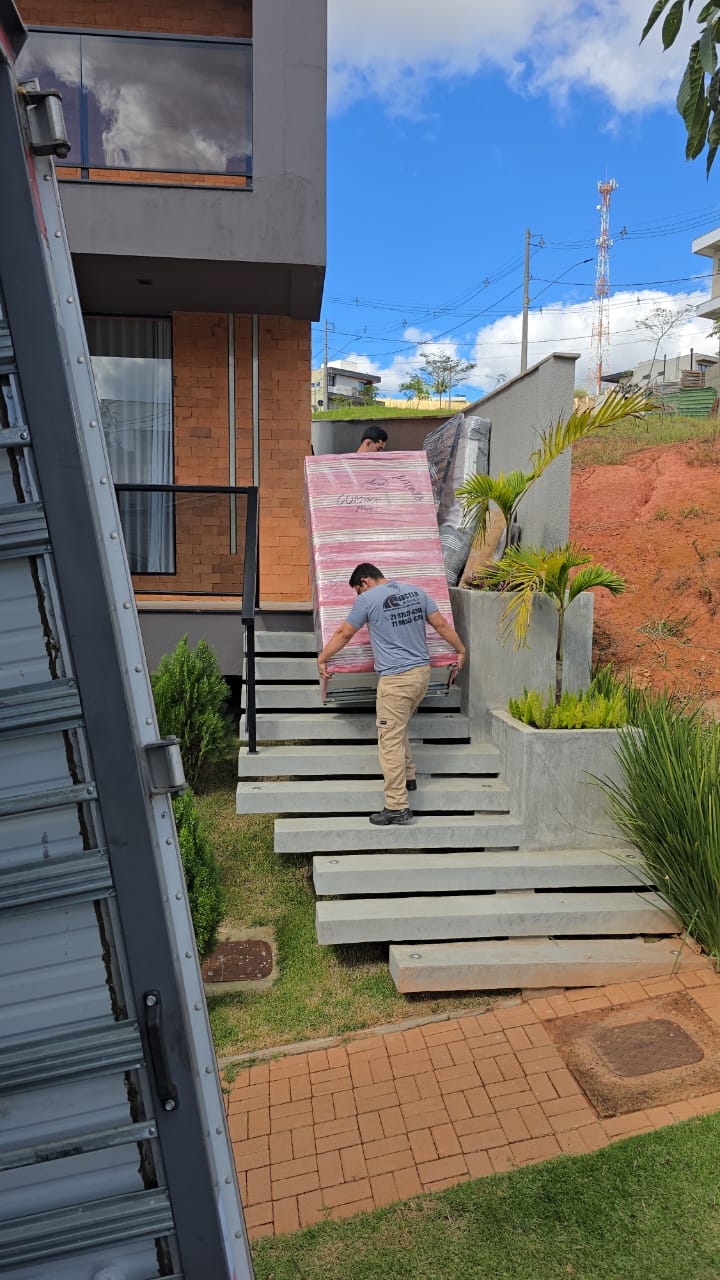 Carregador da equipe com camiseta da Marcelo Mudanças descendo escada externa com um móvel embalado no ombro