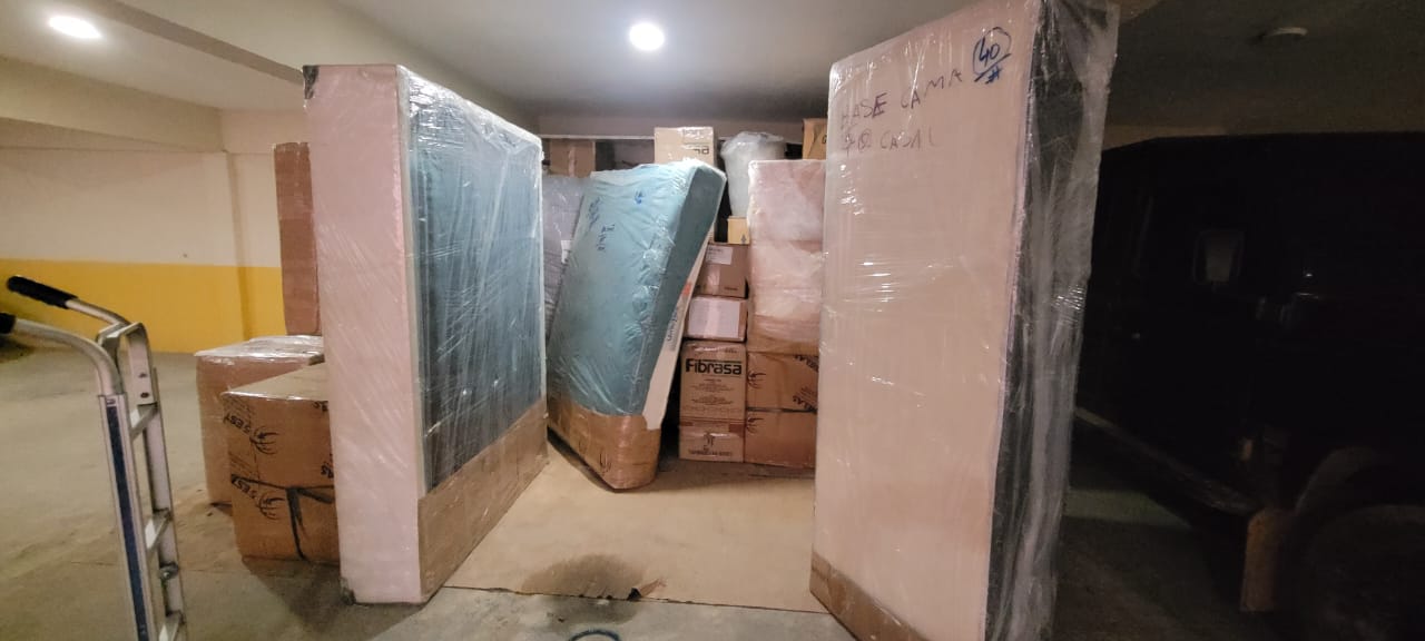 Garagem com base de cama, colchão e caixas embalados em plástico, identificados à caneta