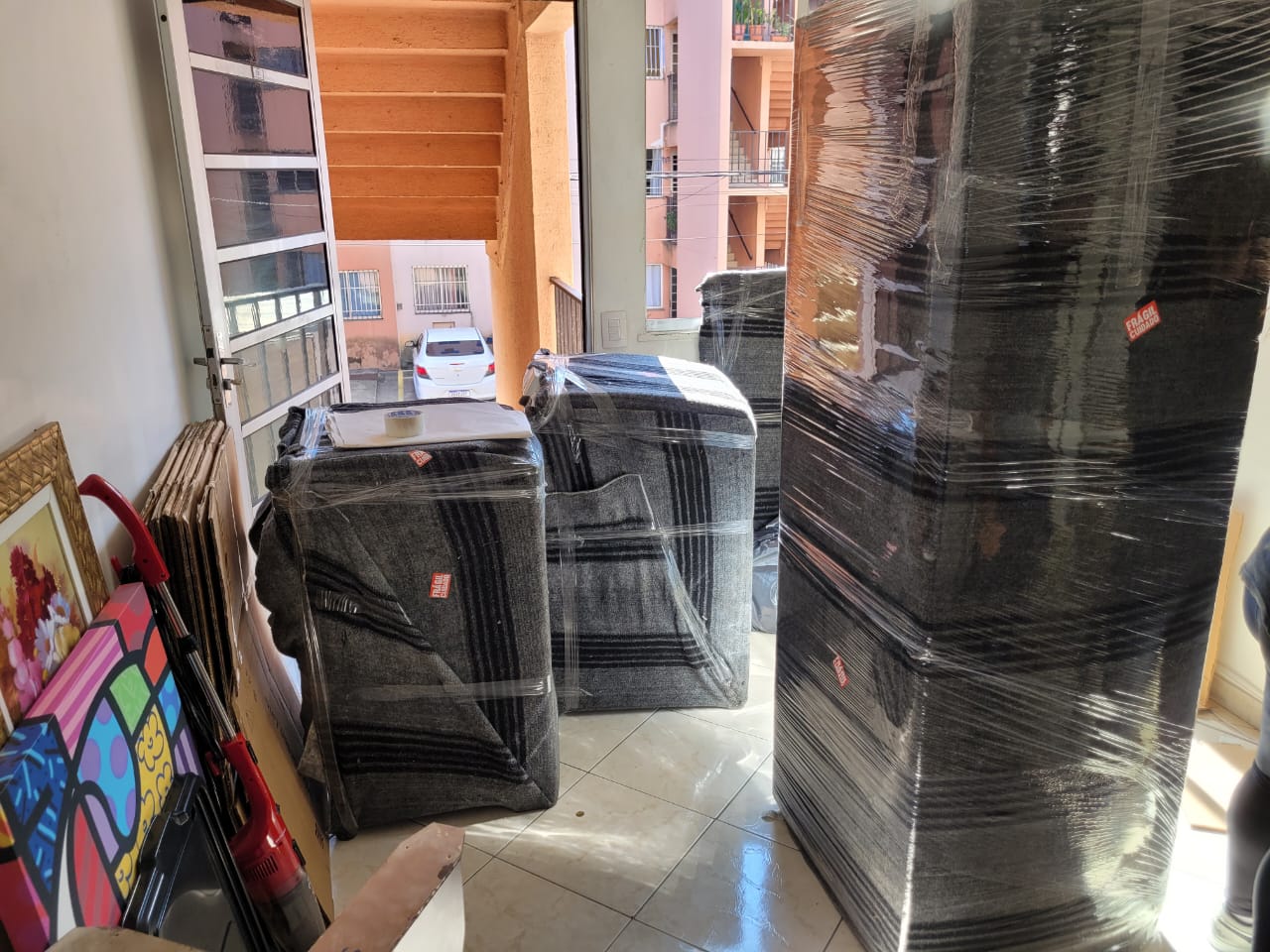 Móveis enrolados em manta cinza listrada e filme plástico na sala de um apartamento, prontos para sair
