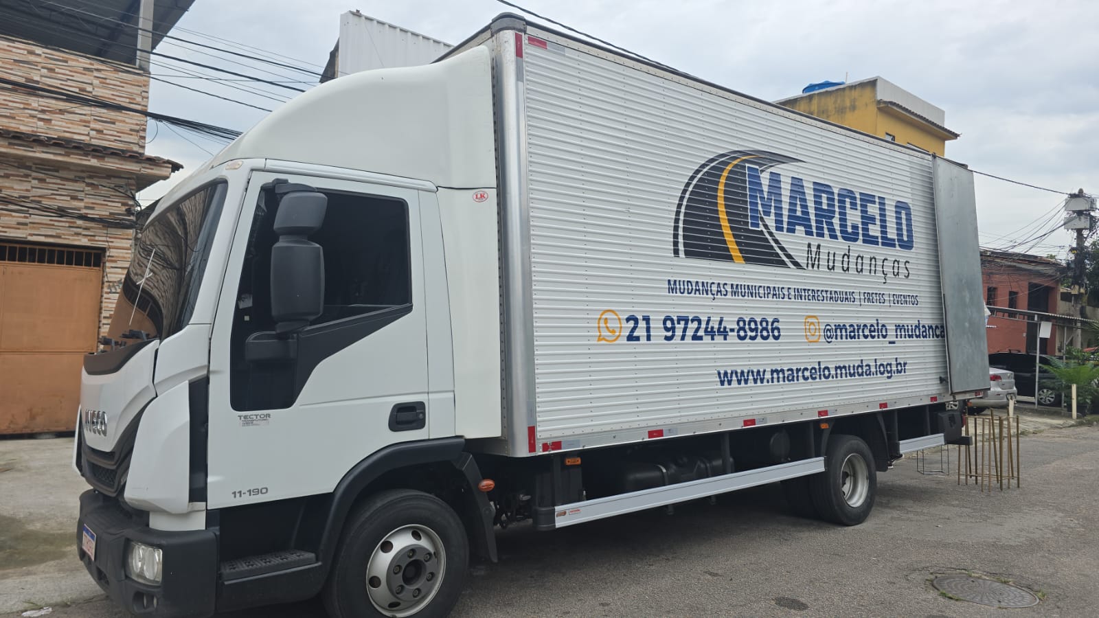 Caminhão baú Iveco branco da Marcelo Mudanças com a logo azul e dourada e o telefone pintados na lateral